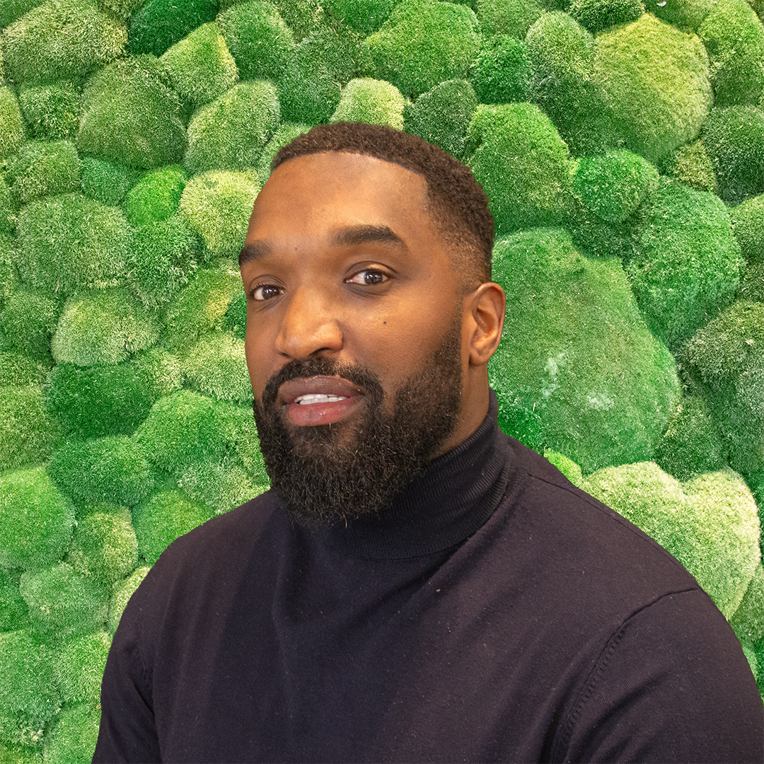 Professional man in black roll-neck against green moss wall.