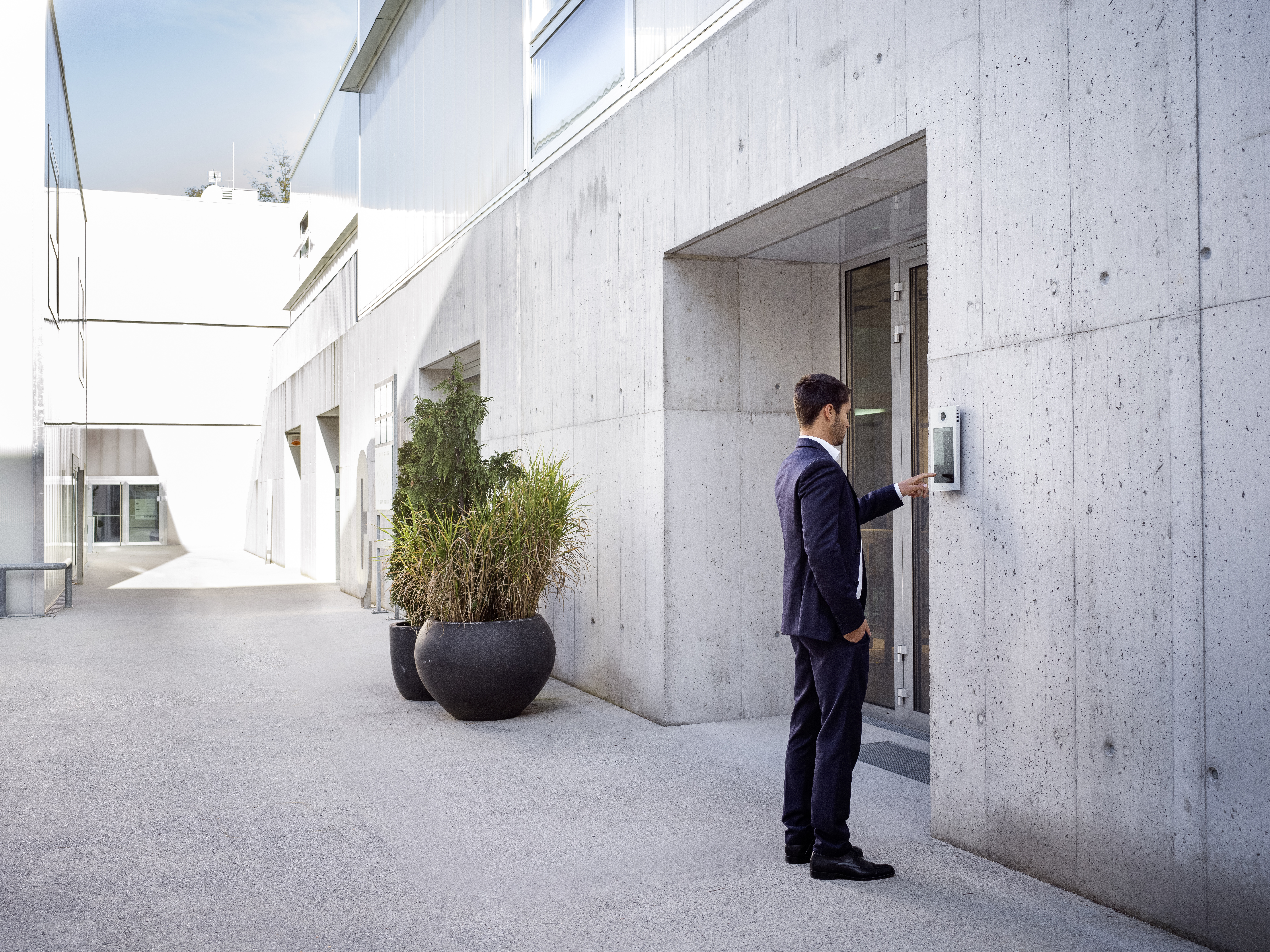 Mann im Anzug bedient Sprechanlage an moderner Betonwand.