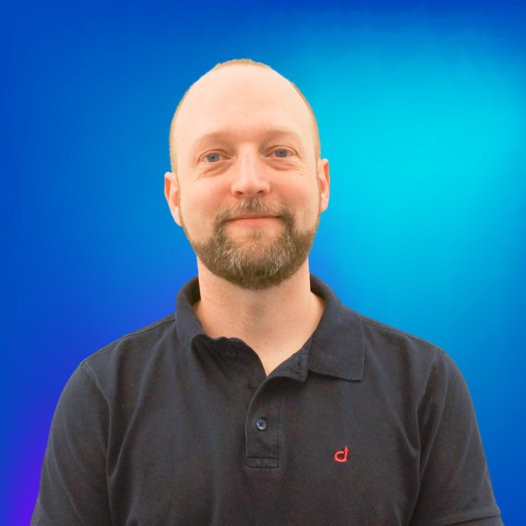 Lächelnder Mann mit Bart im Poloshirt vor blauem Hintergrund.