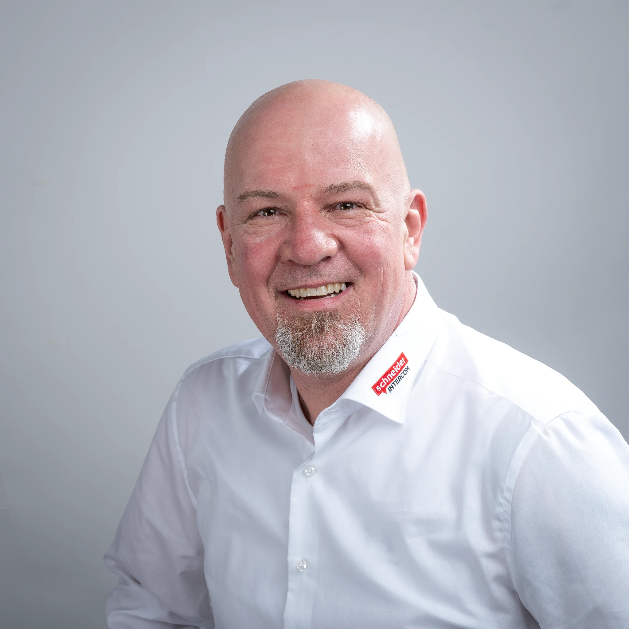 Lächelnder, glatzköpfiger Mann mit Ziegenbart im Schneider INTERCOM Hemd.