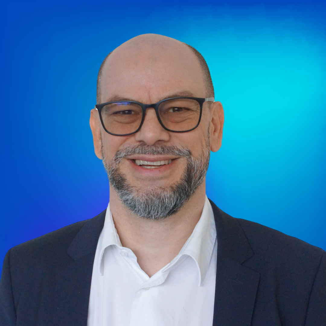 Homme barbu souriant, lunettes, fond bleu.