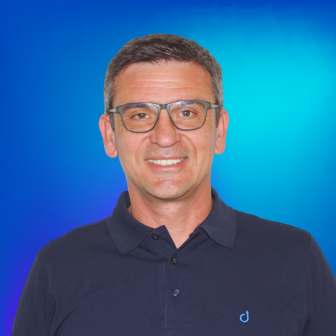 Porträt eines lächelnden Mannes mit Brille in dunkelblauem Poloshirt vor blauem Hintergrund.