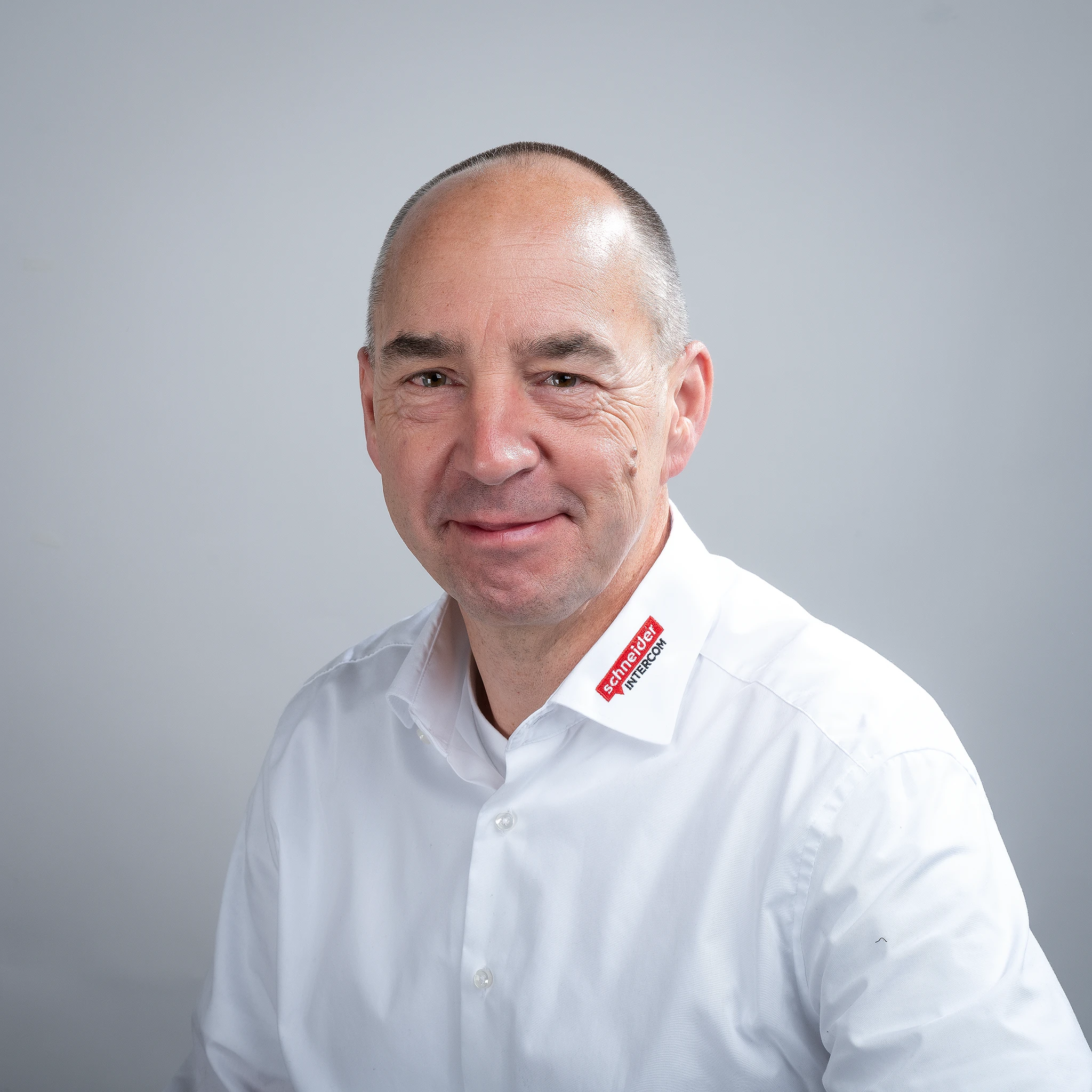 Lächelnder Mann in weißem Hemd mit "schneider INTERCOM" Logo.