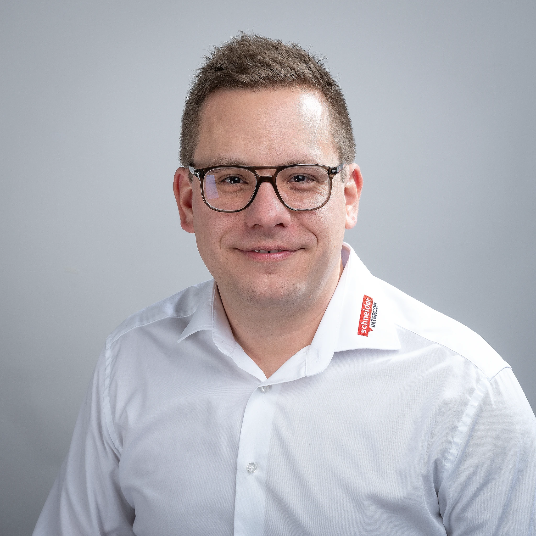 Lächelnder Mann mit Brille und Schneider INTERCOM Logo auf dem Hemd.