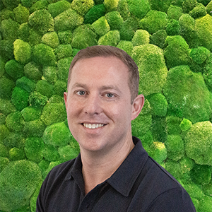 Smiling man in dark polo shirt, green wall.