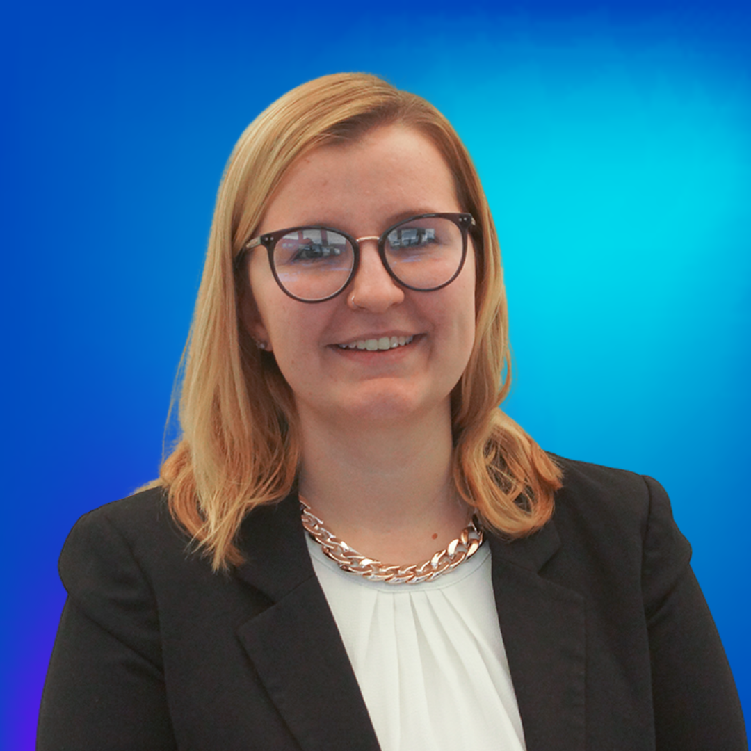 Junge Frau mit blonden Haaren, Brille und goldener Kette lächelt vor blauem Hintergrund.