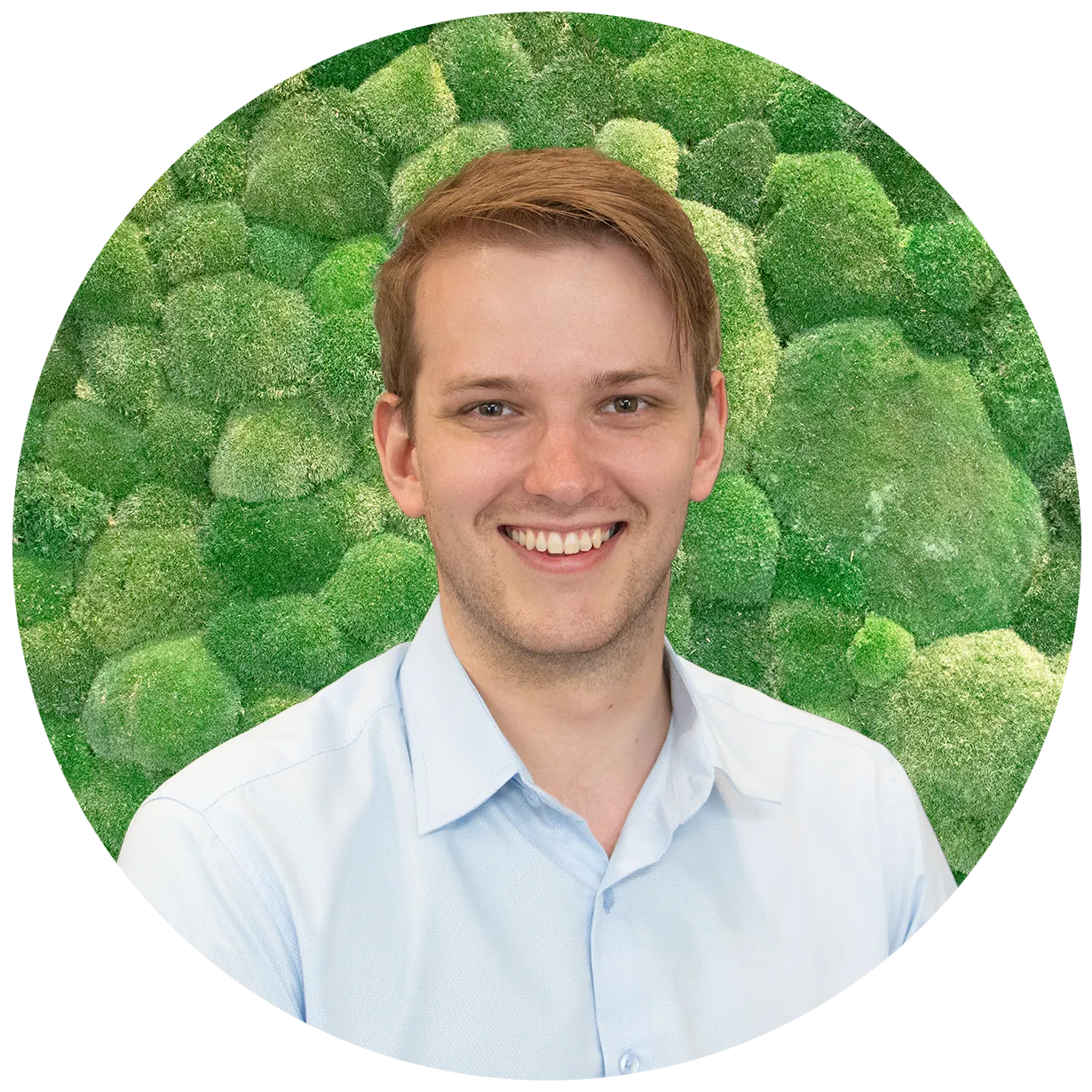 Smiling man in light blue shirt against a green moss wall, cropped in a circle.