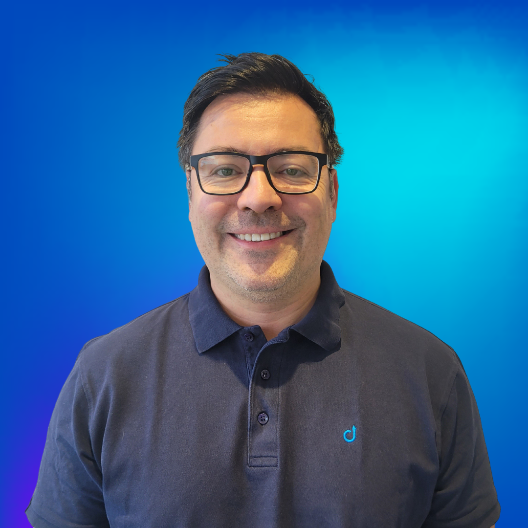 Portrait d'un homme souriant avec des lunettes dans un polo bleu marine sur fond bleu.