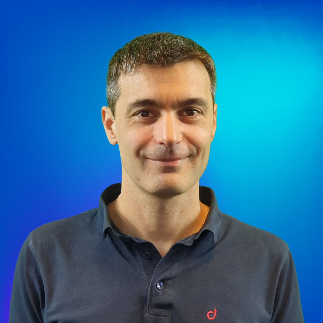 Homme souriant en polo bleu marine sur fond bleu.