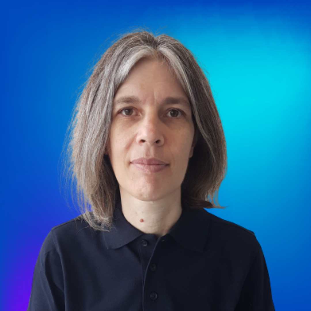 Portrait d'une femme aux cheveux gris et chemise bleue foncée, regardant calmement l'appareil photo sur fond bleu.