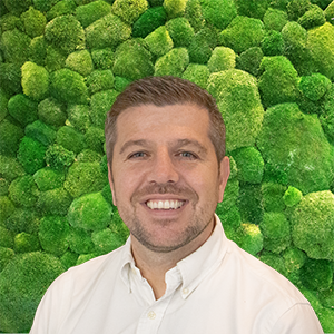 Smiling man in a light shirt against a green textured wall.