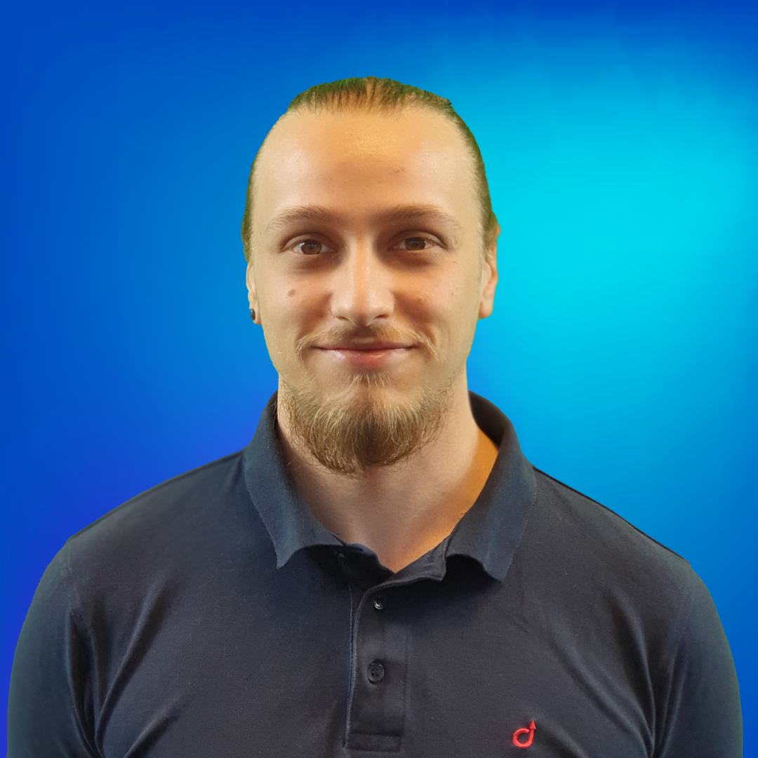 Portrait d'un jeune homme souriant avec barbe et cheveux attachés.