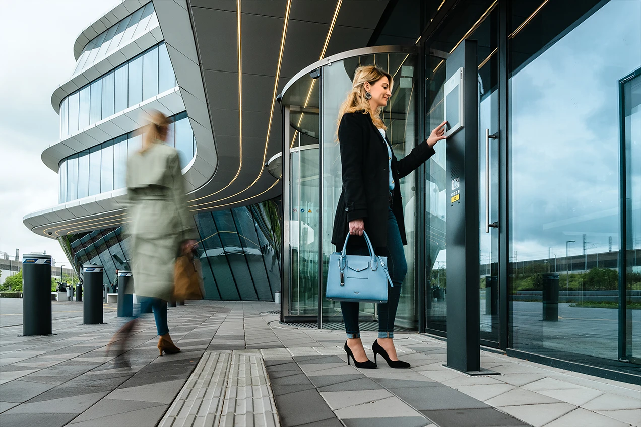 Accès sécurisé : interphone intelligent Femme blonde utilise un interphone tactile à l'entrée d'un bâtiment moderne. Système de communication sécurisé pour l'accès.