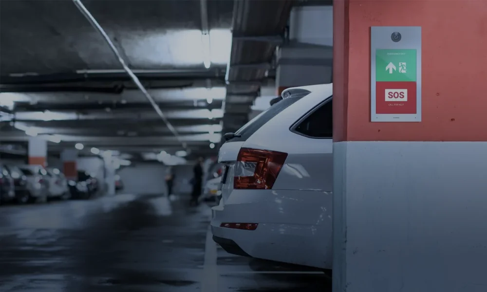 Interphone d'urgence avec bouton SOS et panneaux de sortie dans un parking souterrain.