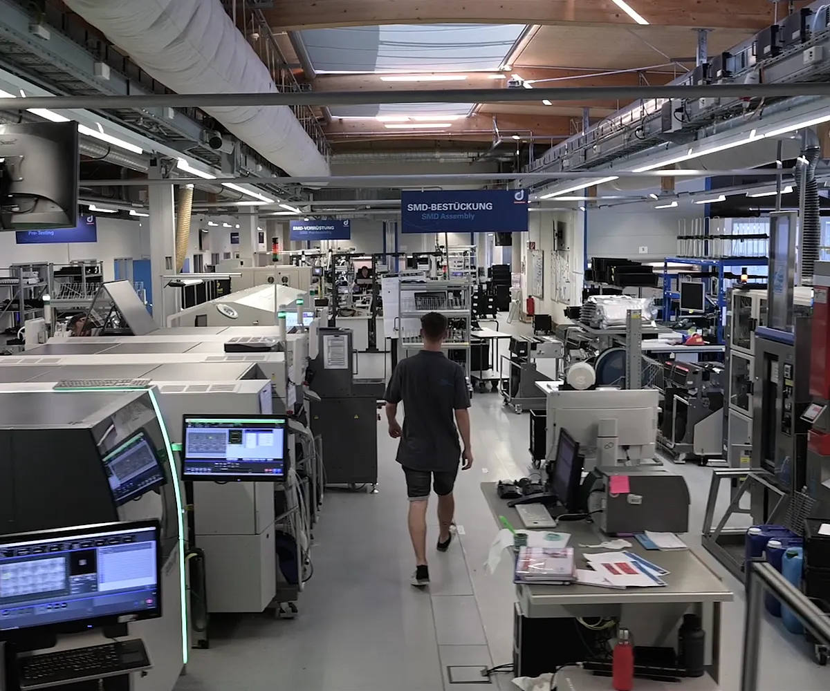 Egy személy sétál egy modern elektronikai gyárban, ahol SMD szerelőgépek vannak.