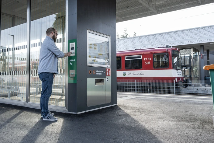 Uomo usa terminale interfonico in stazione Uomo su un binario della stazione preme un pulsante SOS su un interfonico vicino a un orario acustico.