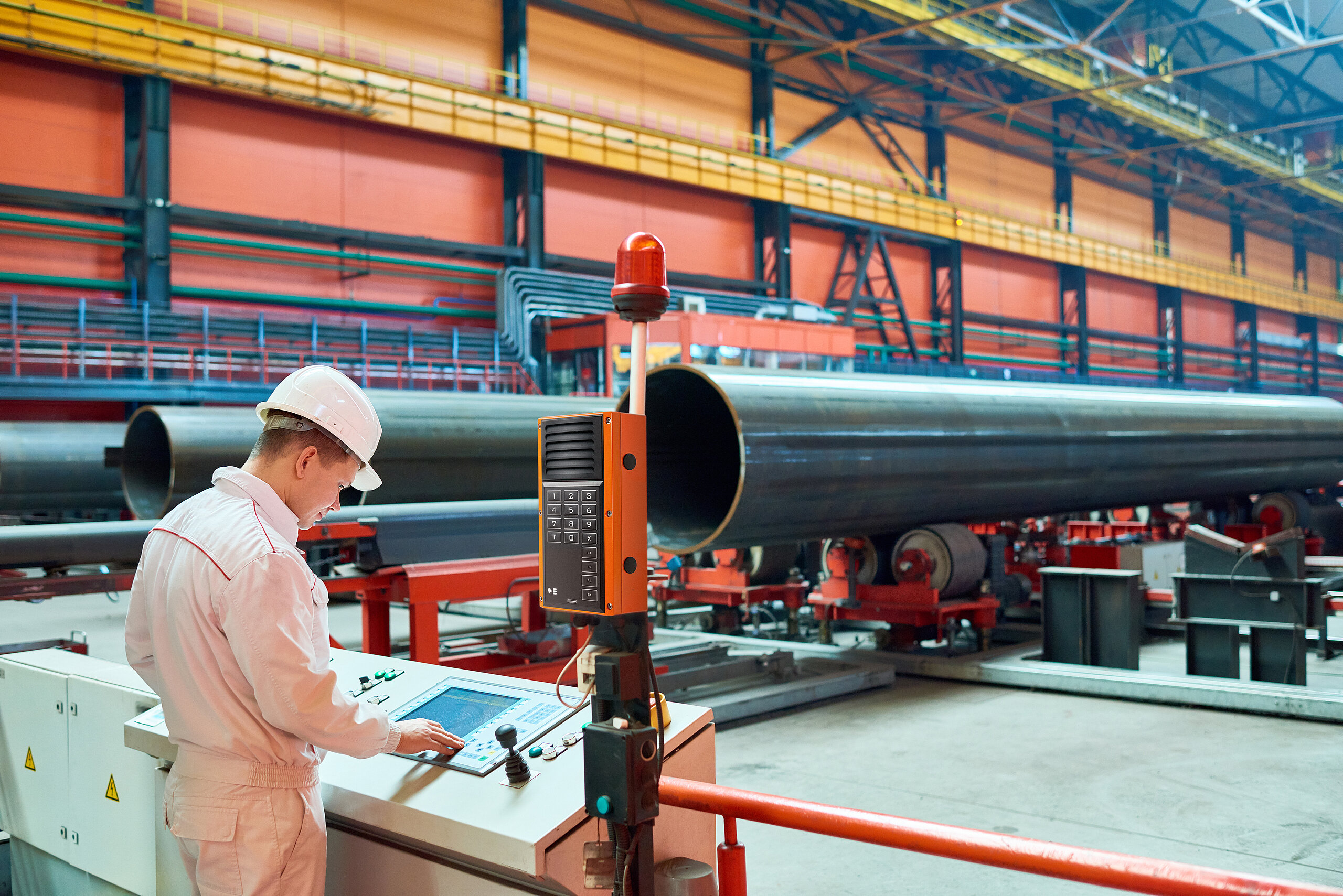 Operatore in fabbrica con terminale interfonico e macchinari pesanti.