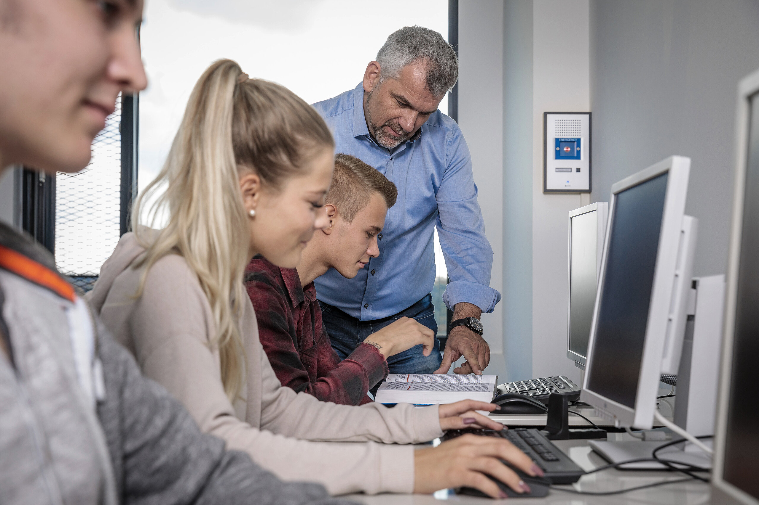 Docente aiuta studenti in laboratorio; sistema interfonico a parete.