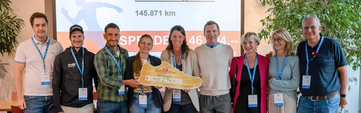 Charity Run Success Celebrated Nine people celebrating a charity run donation of €46,294, holding a large shoe cutout.