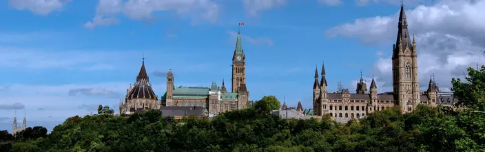 Parliament buildings in Ottawa, Peace Tower, flag, blue sky, green trees.