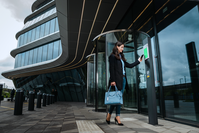 Donna usa lo smartphone per aprire una porta tramite un terminale interfonico moderno all'ingresso di un edificio.