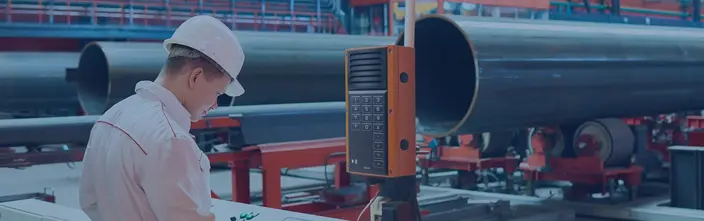 Worker at control panel next to an orange industrial intercom in a factory.
