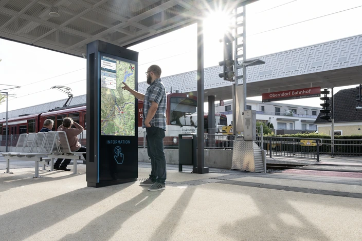 Fahrgast an Bahnhofs-Info-Säule Mann bedient interaktive Infotafel am Bahnhof Oberndorf mit Karte.