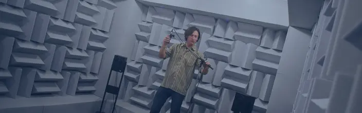 Sound Testing in Acoustic Lab Man adjusting microphone in a soundproof room with patterned walls and speakers.