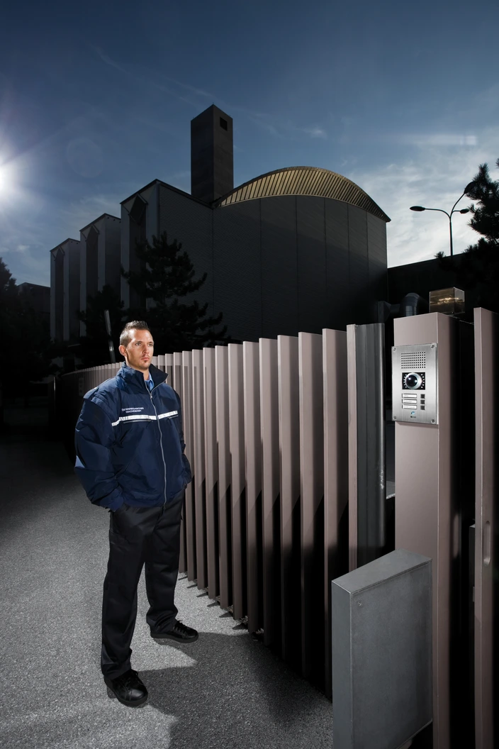 Secure Intercom for Business Access Uniformed security officer beside a modern gate with an intercom at a corporate building entrance.