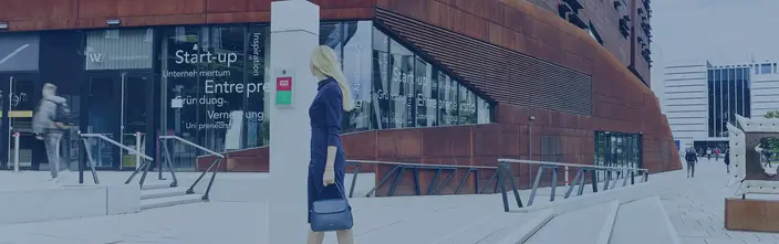 Woman by an intercom on a modern campus building with a rust-coloured facade.