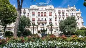 Fachada del Grand Hotel y Jardín Elegante edificio 'Le Grand Hotel' con jardines, fuente y árboles en un día soleado.