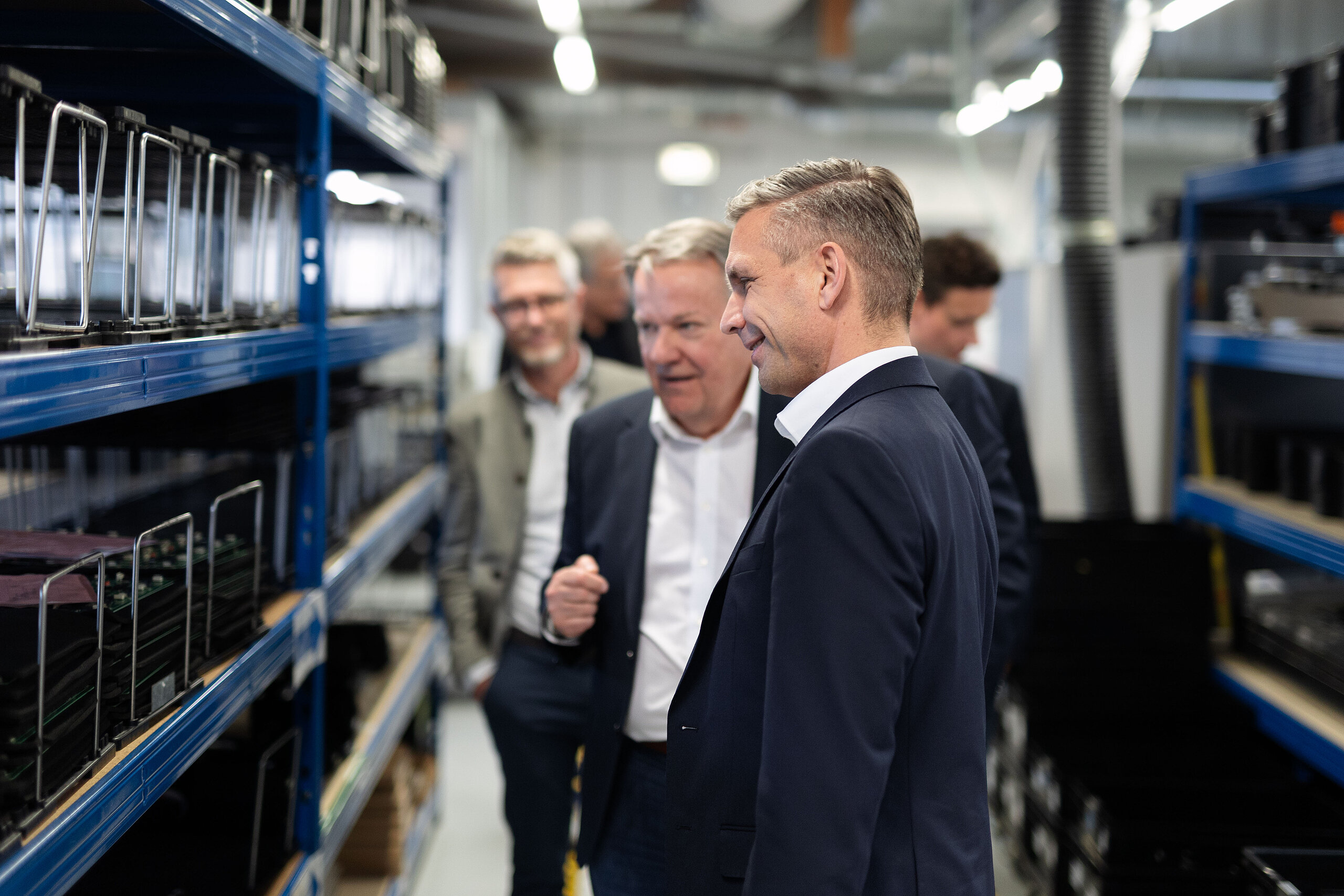 Hombres inspeccionando unidades de interfonía en estantes azules de un almacén.