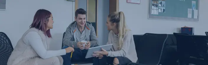 Group discussion with tablet Three young people discuss, one with a tablet, one with a mug, in a bright office.