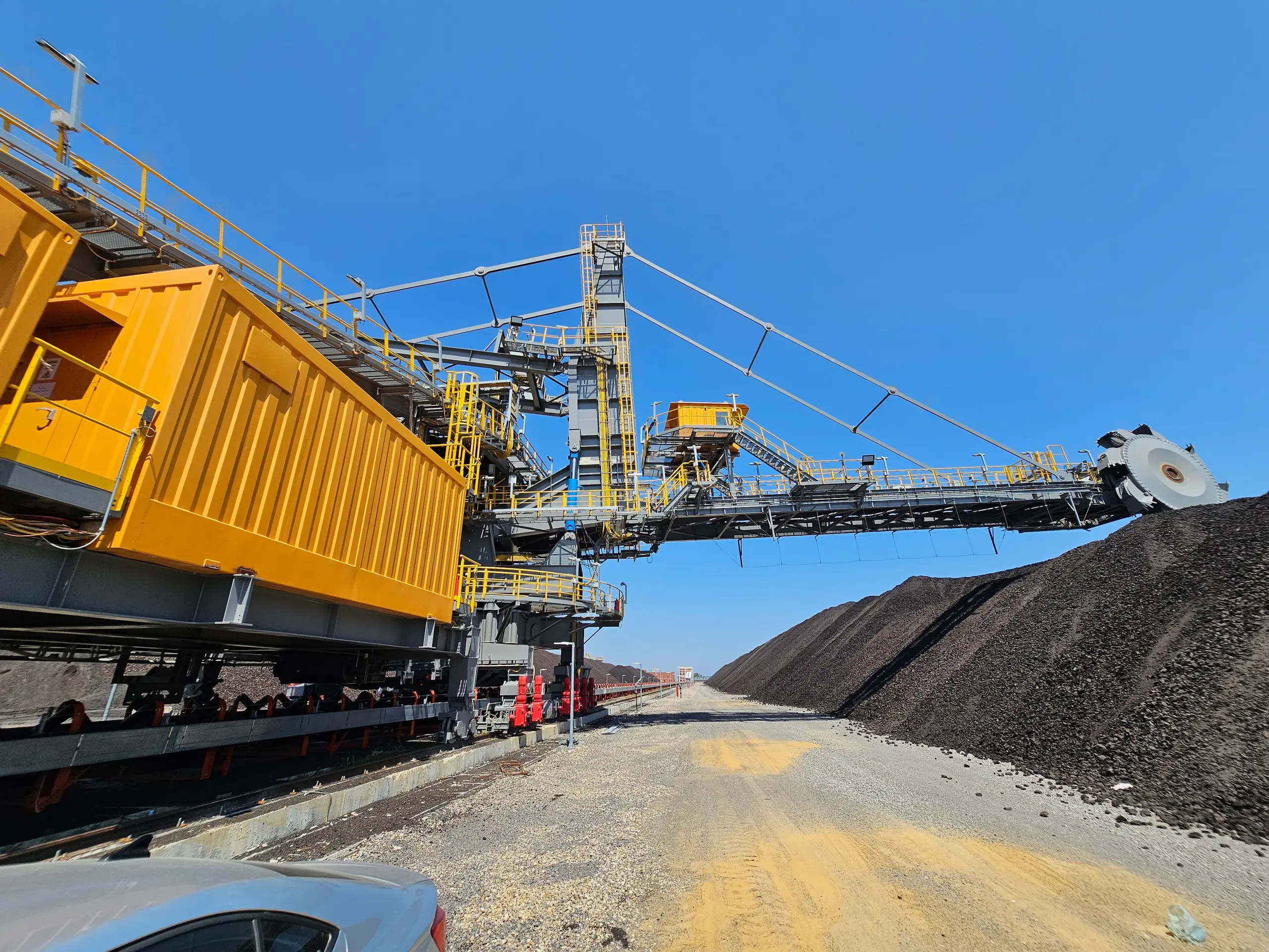 Large stacker with extended conveyor system beside material piles under blue sky Large stacker with conveyor system in industrial operation