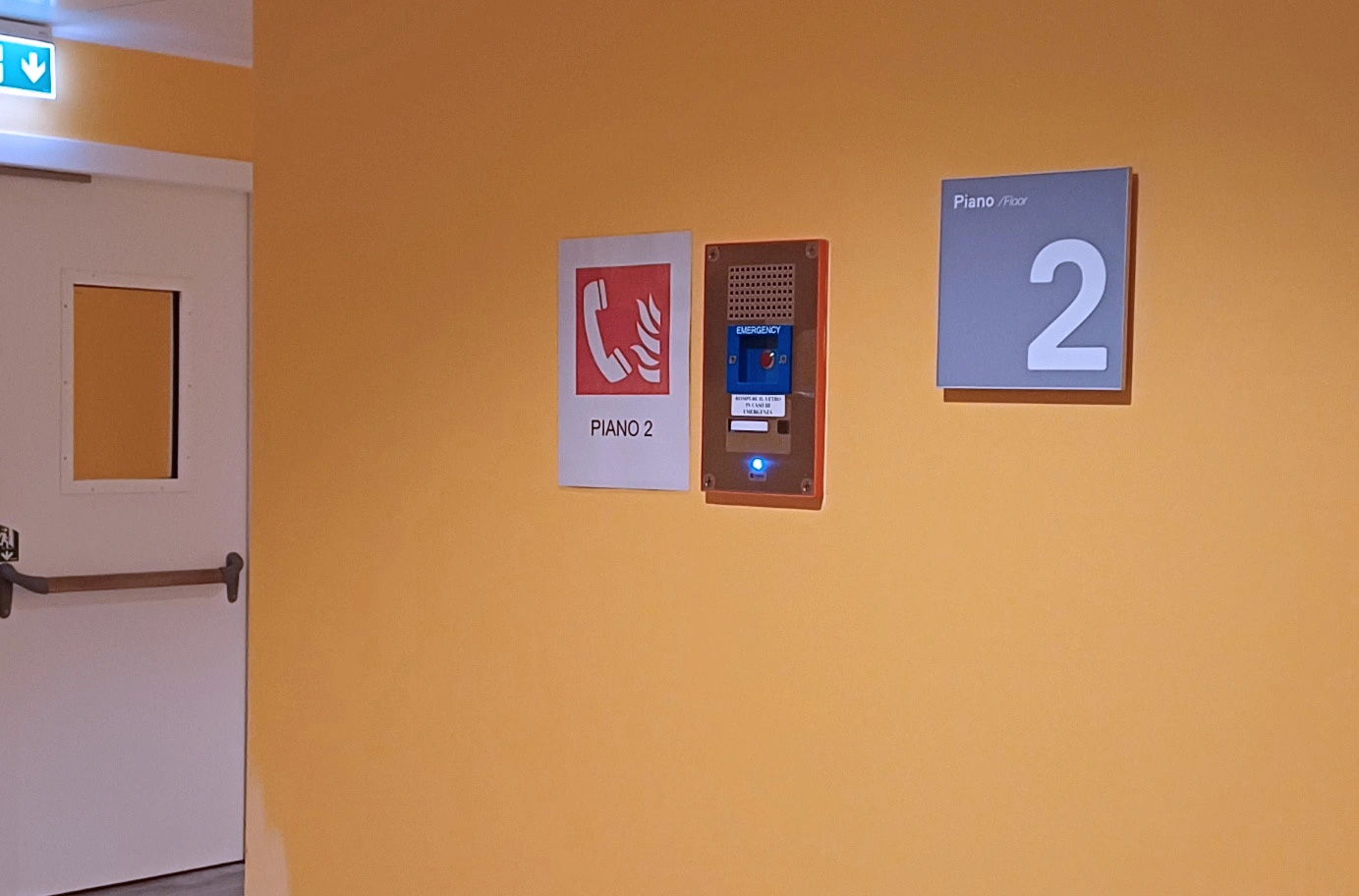 Wall-mounted hospital intercom and emergency call sign on corridor wall beside exit door