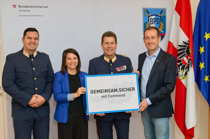 Vier Personen, darunter Uniformierte, halten ein 'GEMEINSAM.SICHER mit Commend'-Schild.