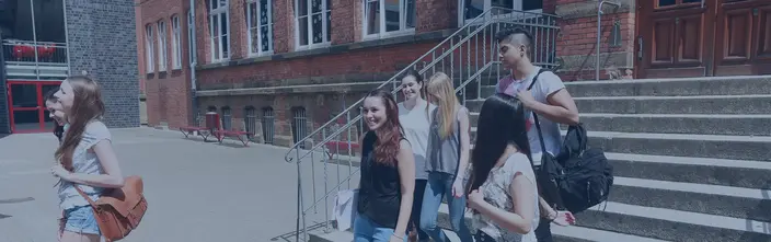 Diverse students leaving a brick school building, smiling in the sunshine.