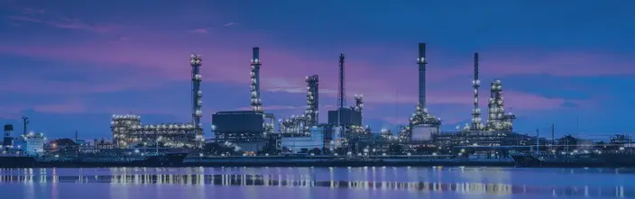 Raffineria al Tramonto: Terminali Interfonici Veduta notturna di una grande raffineria industriale con alte torri, luci e riflessi sull'acqua. Navi ormeggiate.