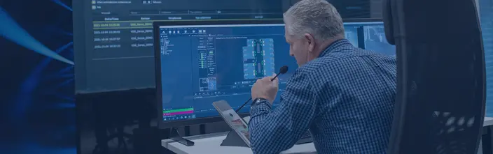 Man with microphone at control desk, viewing security system and floor plans on multiple monitors.