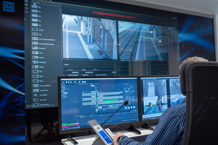 Sala di controllo per sicurezza ferroviaria Operatore in sala di controllo monitora binari, telecamere e sistemi interfonici.