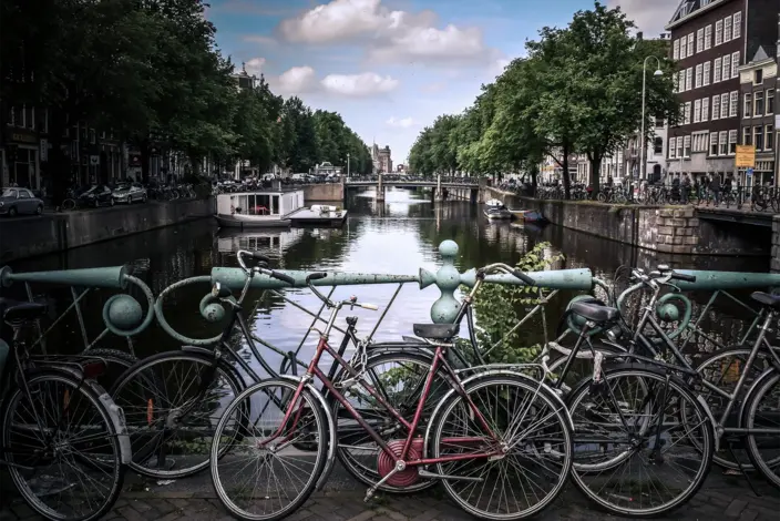 Amsterdamer Grachtenblick mit Fahrrädern Fahrräder parken an einem Brückengeländer mit Blick auf eine Amsterdamer Gracht und Gebäude.