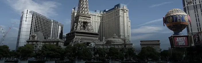 Paris Las Vegas hotel with Eiffel Tower replica, Bally's, and a hot air balloon, under a blue sky.